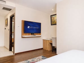 Una habitació d'hotel amb un llit, una taula de treball, una cadira, un televisor penjat a la paret i un quadre a la paret.