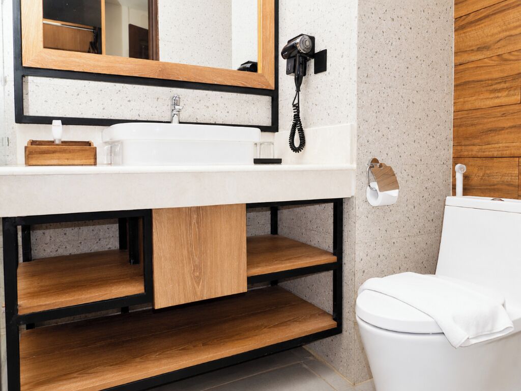 A bathroom with a white sink, wooden shelves, a mirror, and a toilet.