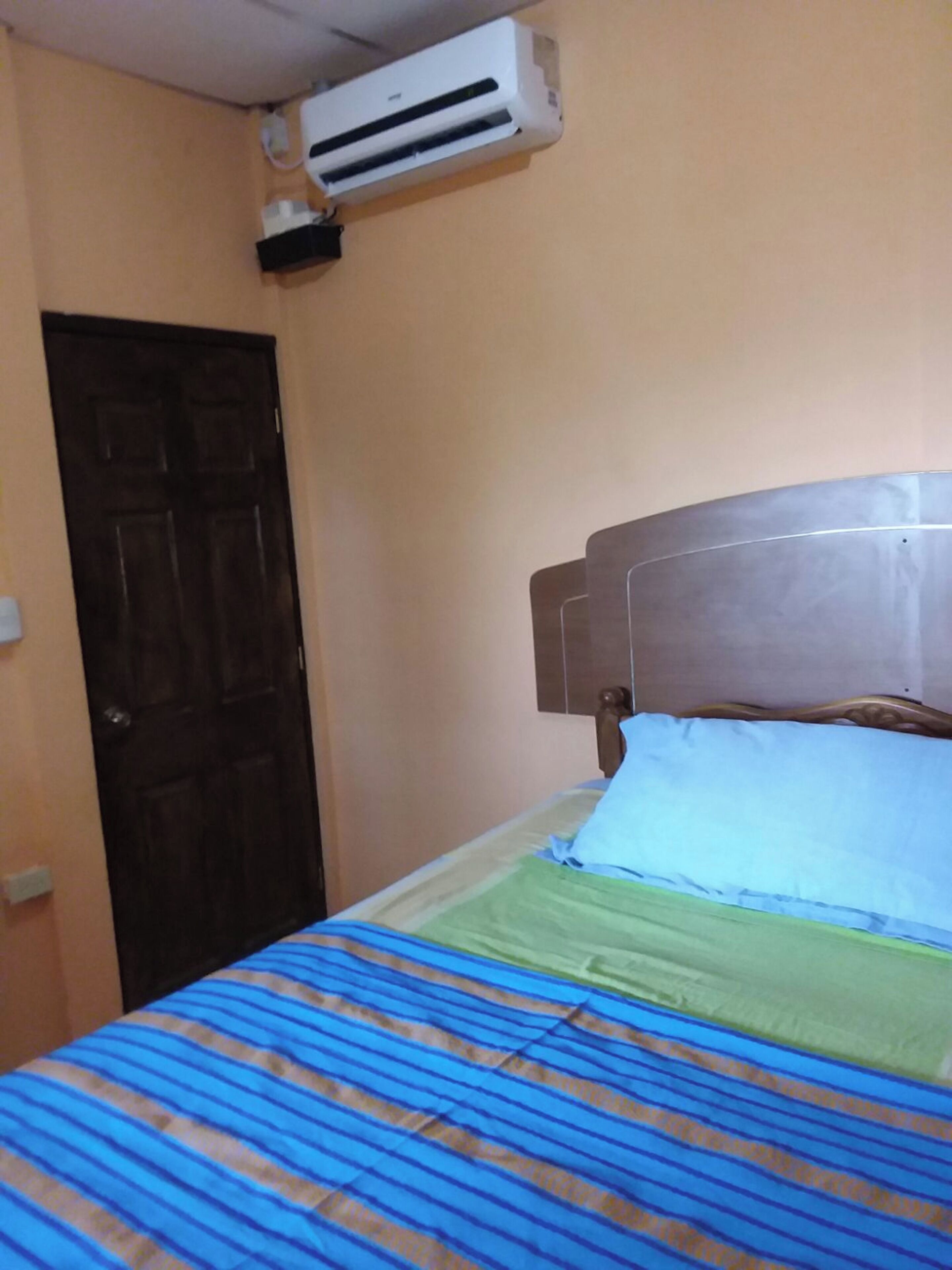 A room with a bed, an air conditioning unit, a door, and a wall.