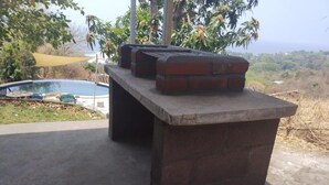 A concrete outdoor bar with a brick top, a pool in the background, and a view of a hilly landscape. - Room-el Zonte Tiki Surfer Beds Steps f (Chiltiupan)