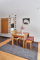 Un comedor con una mesa de madera, sillas, un florero con flores y un espejo en la pared.