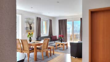 A modern living room with a dining area, a sofa, and a view of the outdoors.