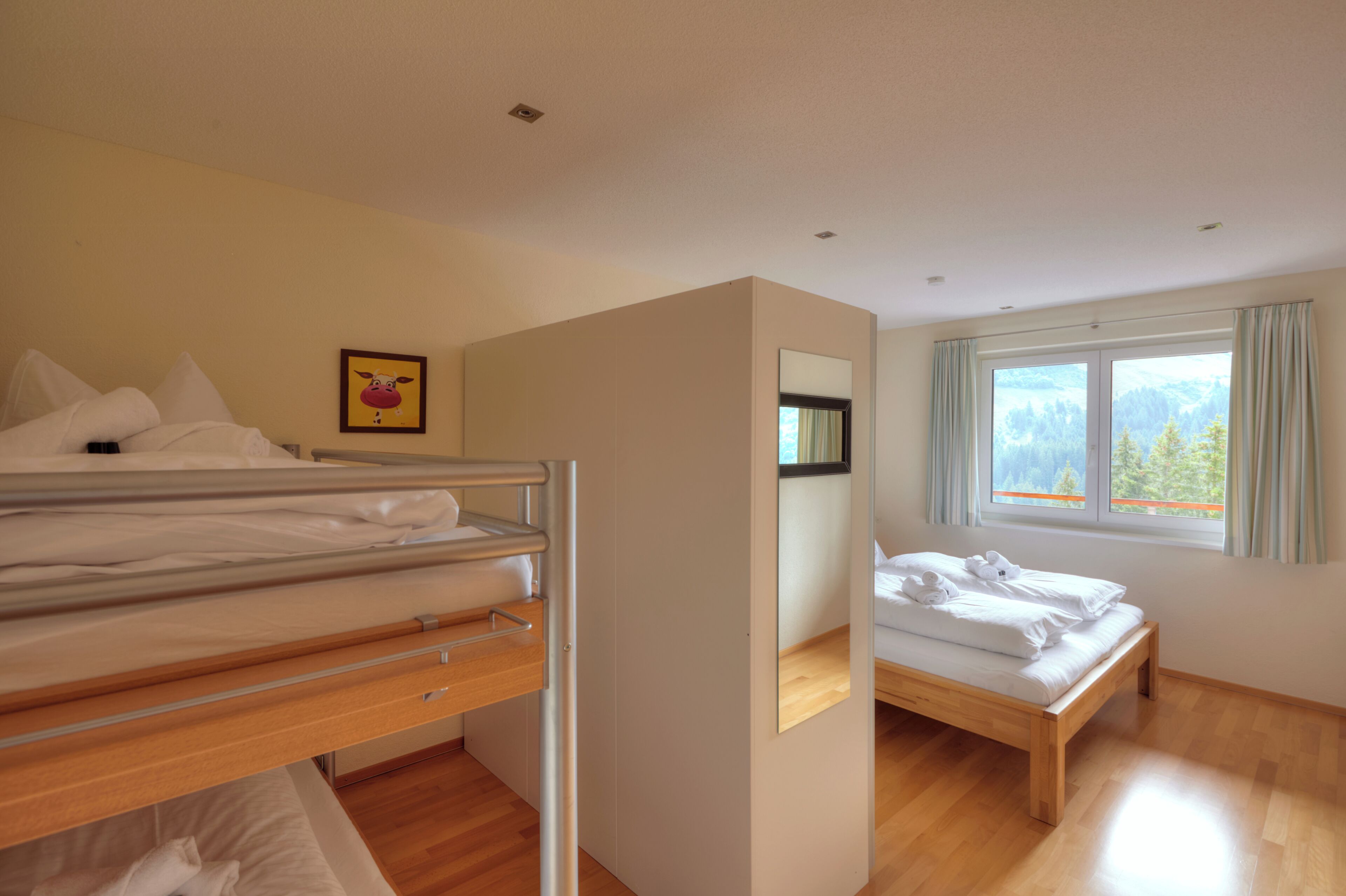 A bedroom with a bunk bed, a single bed, a window with a view, and a mirror.
