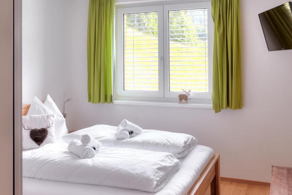 A bedroom with two beds, a window with green curtains, a small deer decoration, and a mounted television.