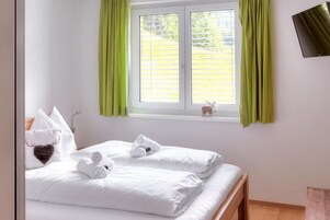 Un dormitorio con dos camas, una ventana con cortinas verdes, una decoración de ciervo pequeño y un televisor montado.