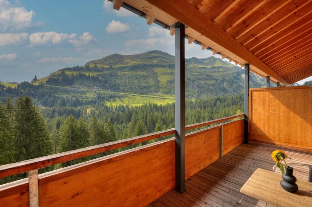 A wooden balcony with a view of a forested valley and mountains.