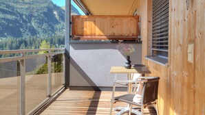 Ein Balkon mit Holztisch und Stuhl, einer Blumenvase und Blick auf eine Berglandschaft.