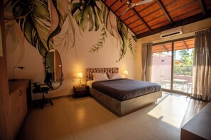 Un dormitorio con cama, dos lámparas de noche, un espejo, un escritorio y vistas al exterior a través de una puerta corrediza de vidrio.
