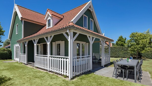 Et grønt hus med en hvid veranda og et spiseområde med bord og stole.