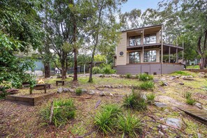 A modern two-story house with a deck, surrounded by a garden with rocks and plants. - Gariwerd Family Lodge (Halls Gap)