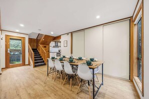 A dining area with a wooden table, white chairs, and a staircase leading to a kitchen.