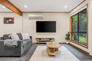 A living room with a grey sofa, a coffee table, a flat-screen TV, a large window, and a potted plant.