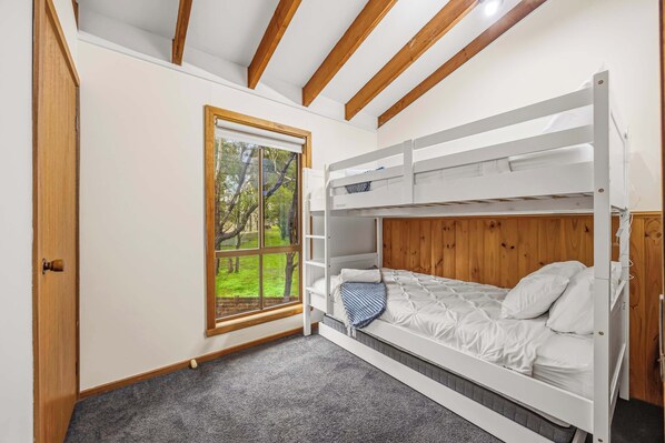 A room with a bunk bed, a window with a view of greenery, and wooden beams on the ceiling.