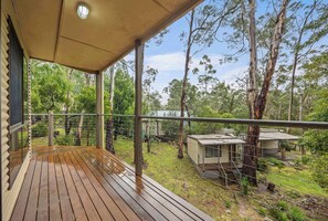 A wooden deck with a metal railing, overlooking a garden with trees and a small building.
