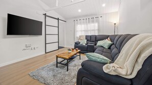 Ett modernt vardagsrum med en platt-TV, en soffa, ett soffbord och ett stort fönster med gardiner.