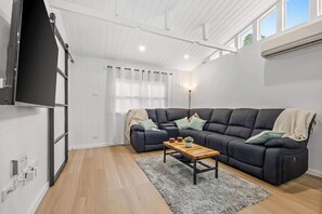 A modern living room with a sectional sofa, a wooden coffee table, and a large flat-screen TV mounted on the wall.