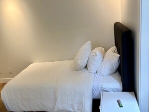Ein Bett mit weißer Bettwäsche und Kissen, ein Nachttisch mit Lampe sowie eine Steckdose an der Wand.