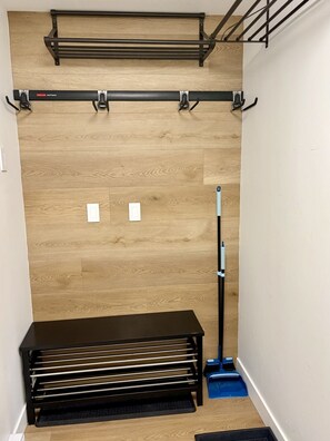 Ein Zimmer mit Holzboden, einer schwarzen Bank, einem Besen und einem an der Wand befestigten Ablagefach.