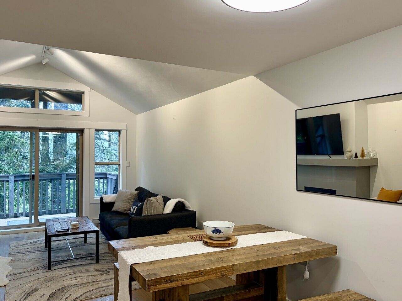 A modern living room with a sofa, a wooden coffee table, a bowl, and a television mounted on the wall.