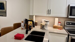 Eine moderne Küche mit weißen Schränken, einem Edelstahlherd, einer Kaffeemaschine und einem Spülbecken.