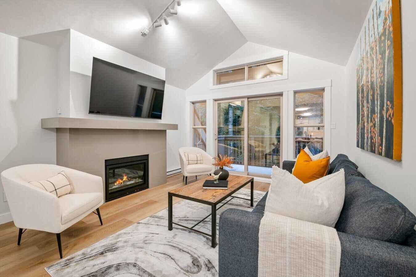 A modern living room with a fireplace, a flat-screen TV, and a sofa with cushions.