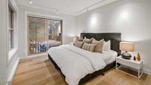 Ein Schlafzimmer mit einem großen Bett, einem Nachttisch, einer Lampe und einer Schiebetür zu einem Balkon.