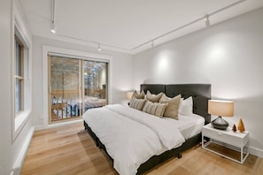 Ein Schlafzimmer mit einem großen Bett, einem Nachttisch, einer Lampe und einer Schiebetür zu einem Balkon.