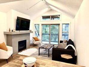 Ein modernes Wohnzimmer mit Kamin, Flachbildfernseher und einem großen Fenster mit Blick auf eine Terrasse.