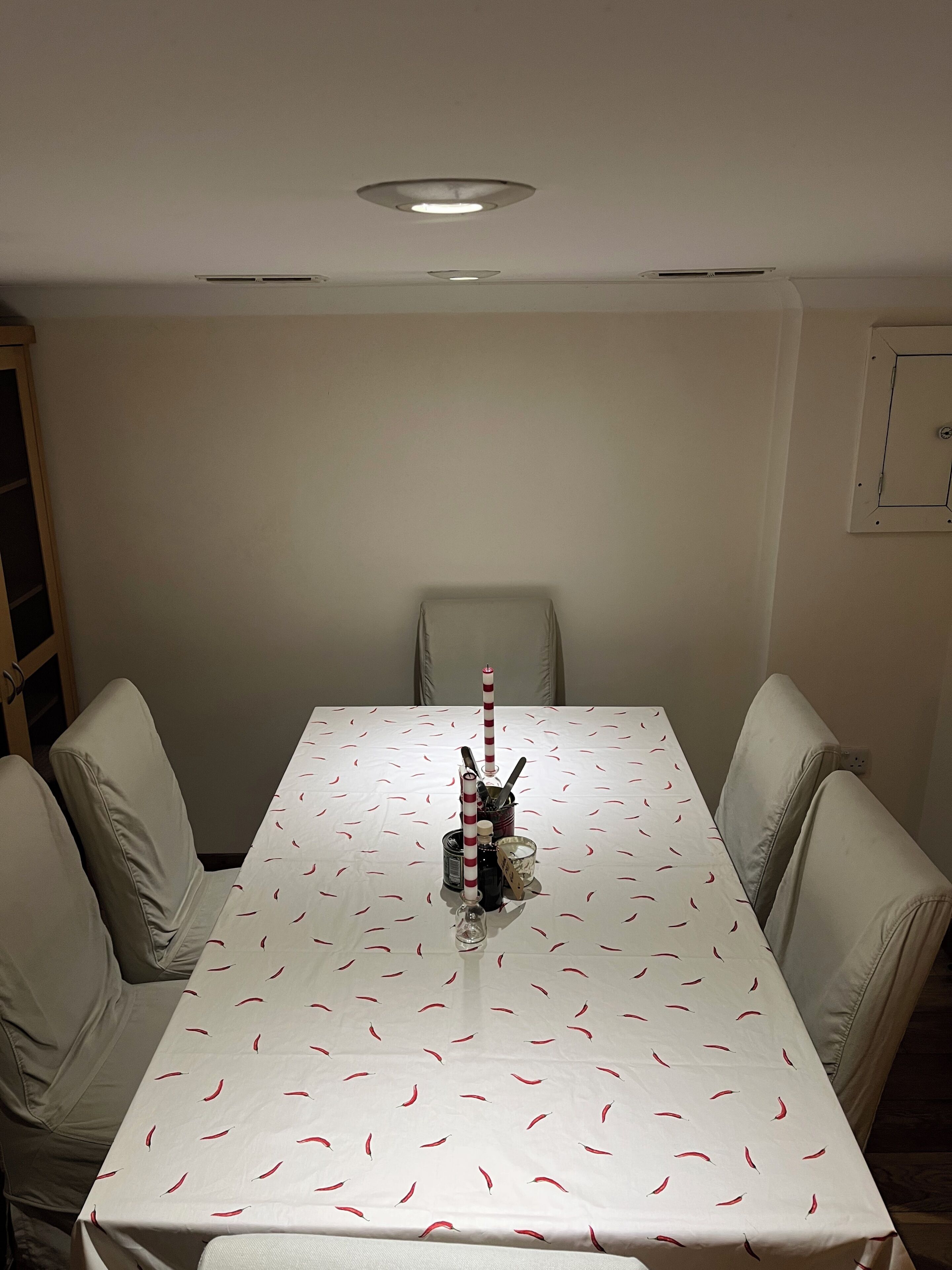 A dining table with a white tablecloth and red chili pepper pattern, surrounded by four beige chairs.