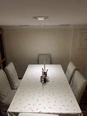 Ein Esstisch mit weißer Tischdecke und einem Muster aus roten Chilischoten, umgeben von vier beigen Stühlen.