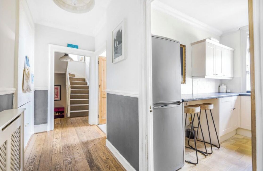 A kitchen with a refrigerator, bar stools, and a staircase leading to another room.
