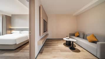 A modern hotel room with a bed, a sofa, a TV, and a small table.