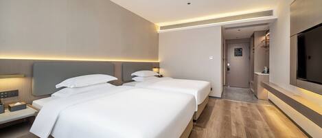 Habitación de hotel con dos camas, televisión, escritorio y baño visible a través de una puerta abierta.