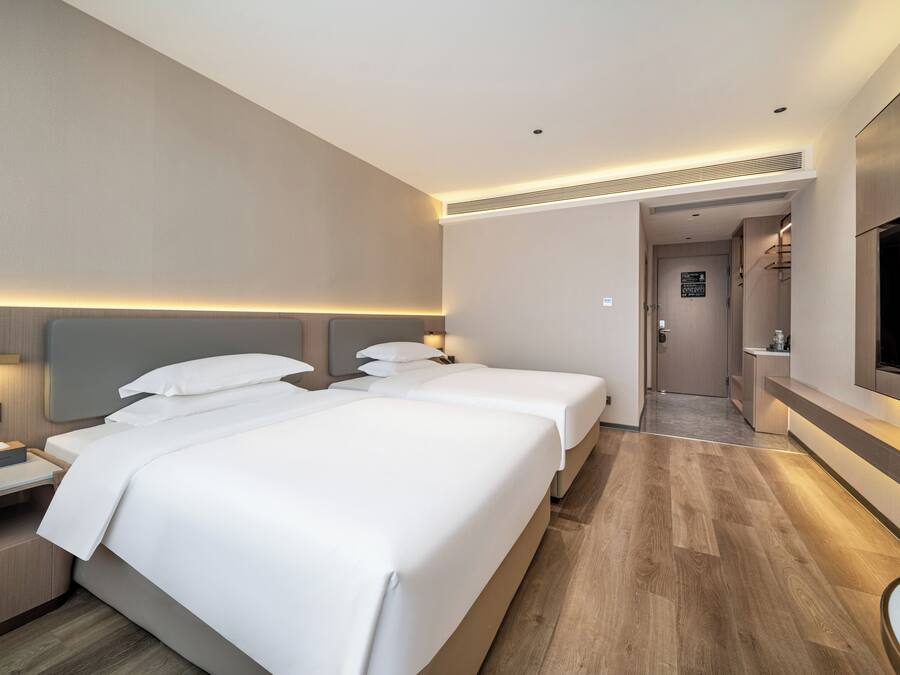 Ein Hotelzimmer mit zwei Betten, einem Fernseher, einem Schreibtisch und einem durch eine offene Tür einsehbaren Badezimmer.
