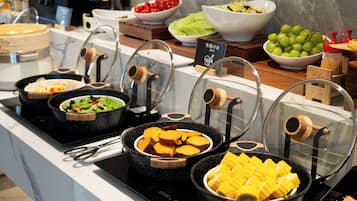 Un buffet proposant une variété de plats, notamment des salades, des fruits et des patates douces.