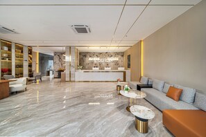 A modern hotel lobby with a reception desk, seating area, and a marble floor.