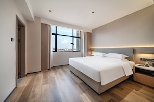Habitación de hotel con una cama grande, un escritorio con lámpara, una ventana con vistas y una puerta.