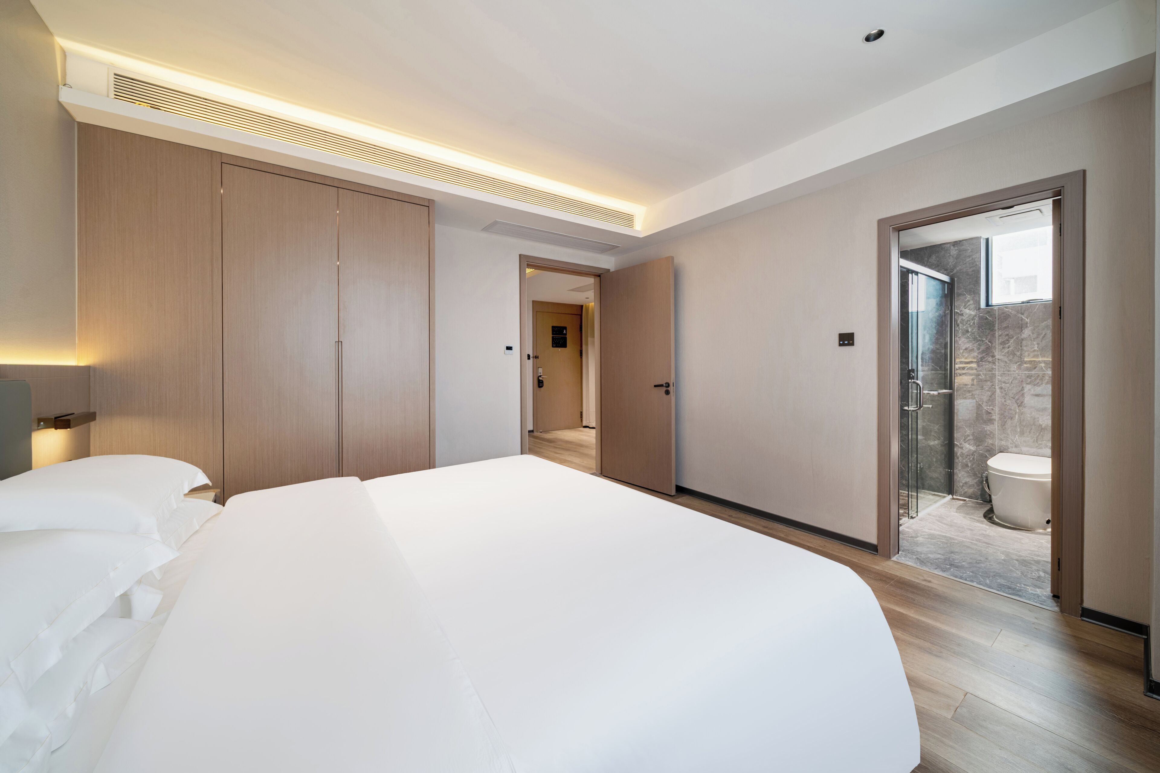 Quarto moderno com cama grande, guarda-roupa de madeira e banheiro com chuveiro de vidro.