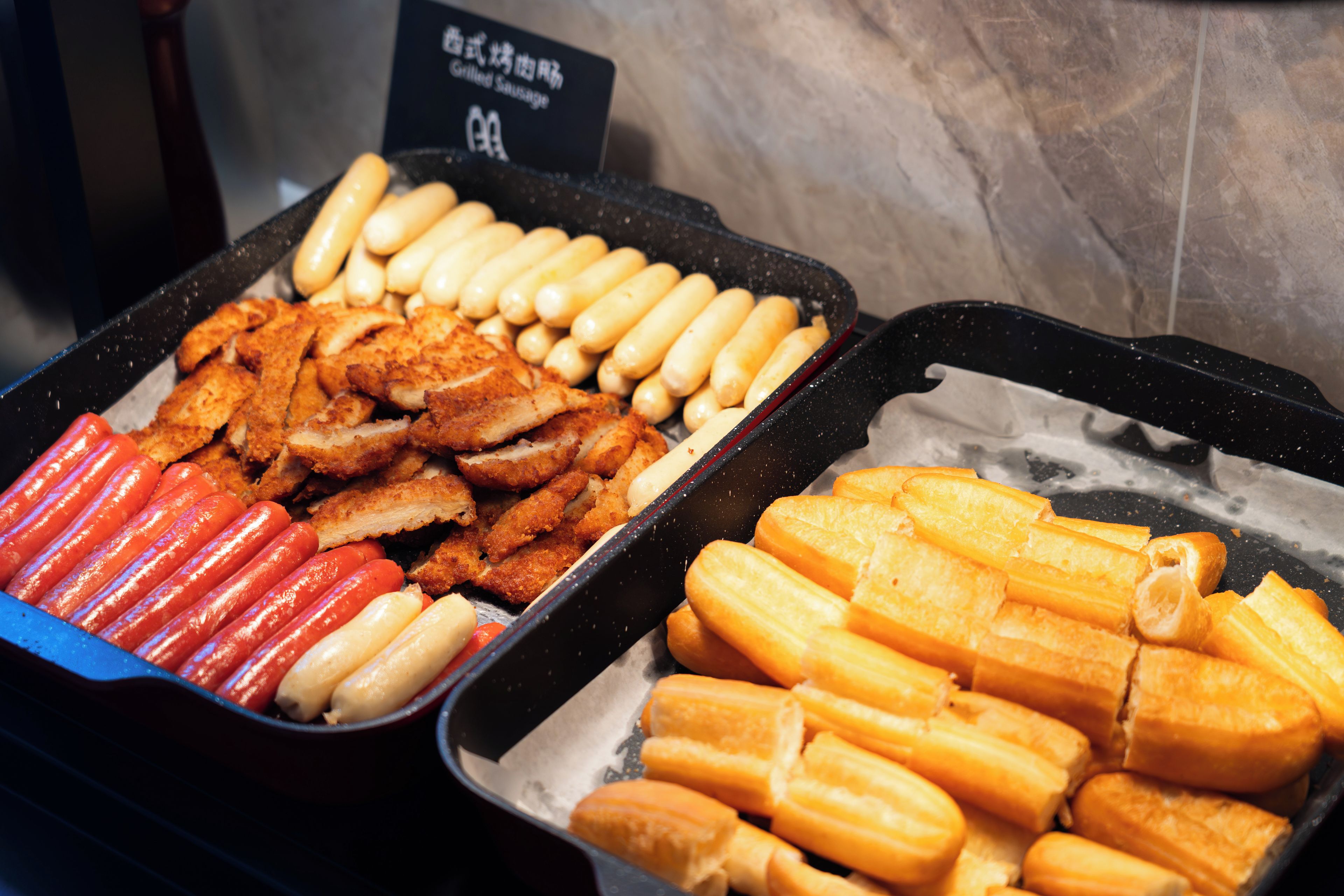 A buffet with various food items including sausages, bread, and fried chicken.