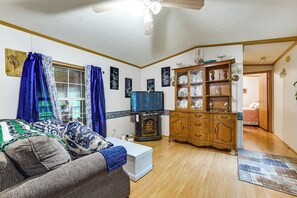 Ein Wohnzimmer mit einer Couch, einem Fernseher, einem Holzkasten und einem Fenster mit Vorhängen.