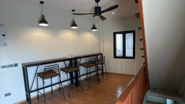 Un comedor con una mesa y sillas, un ventilador de techo, luces colgantes y una escalera.
