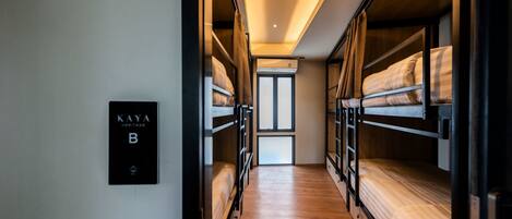 A corridor with bunk beds, a sign reading 'KAYA HERITAGE B', and a view of a door at the end.