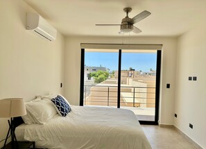 A bedroom with a bed, a ceiling fan, an air conditioning unit, and a view of the cityscape through a large window. - 2BR Vistana Estates Townhome 5min to Downtown Cabo (El Tezal, Cabo San Lucas)