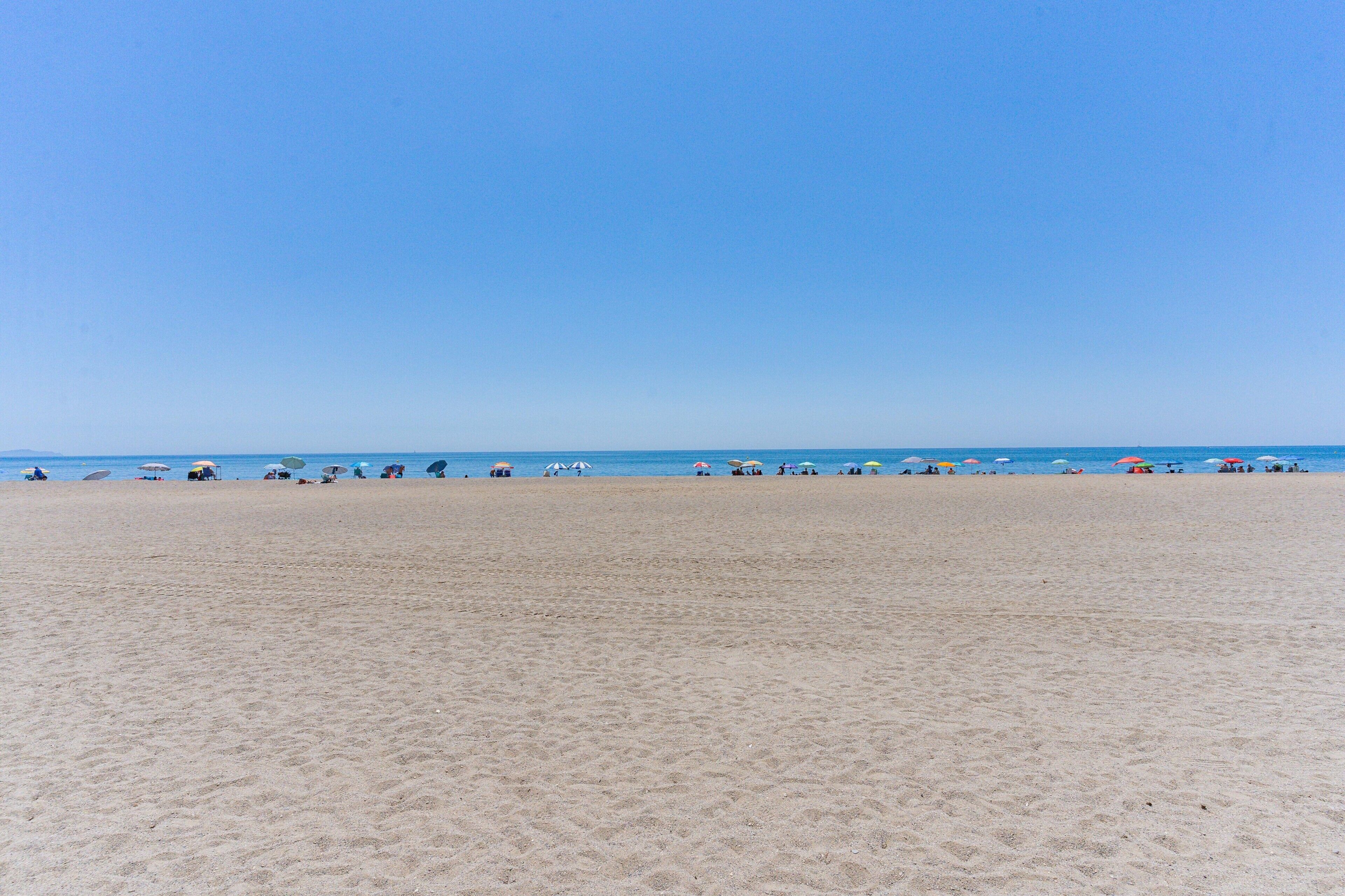 A wide sandy beach with umbrellas and people.