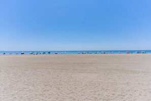 A wide sandy beach with umbrellas and people. - 'Club Tropicana' Apartment with Sea View, Private Pool, and Wi-Fi (Roquetas de Mar)