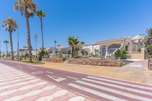 A street with palm trees, a pedestrian crossing, and a building with a stone facade.