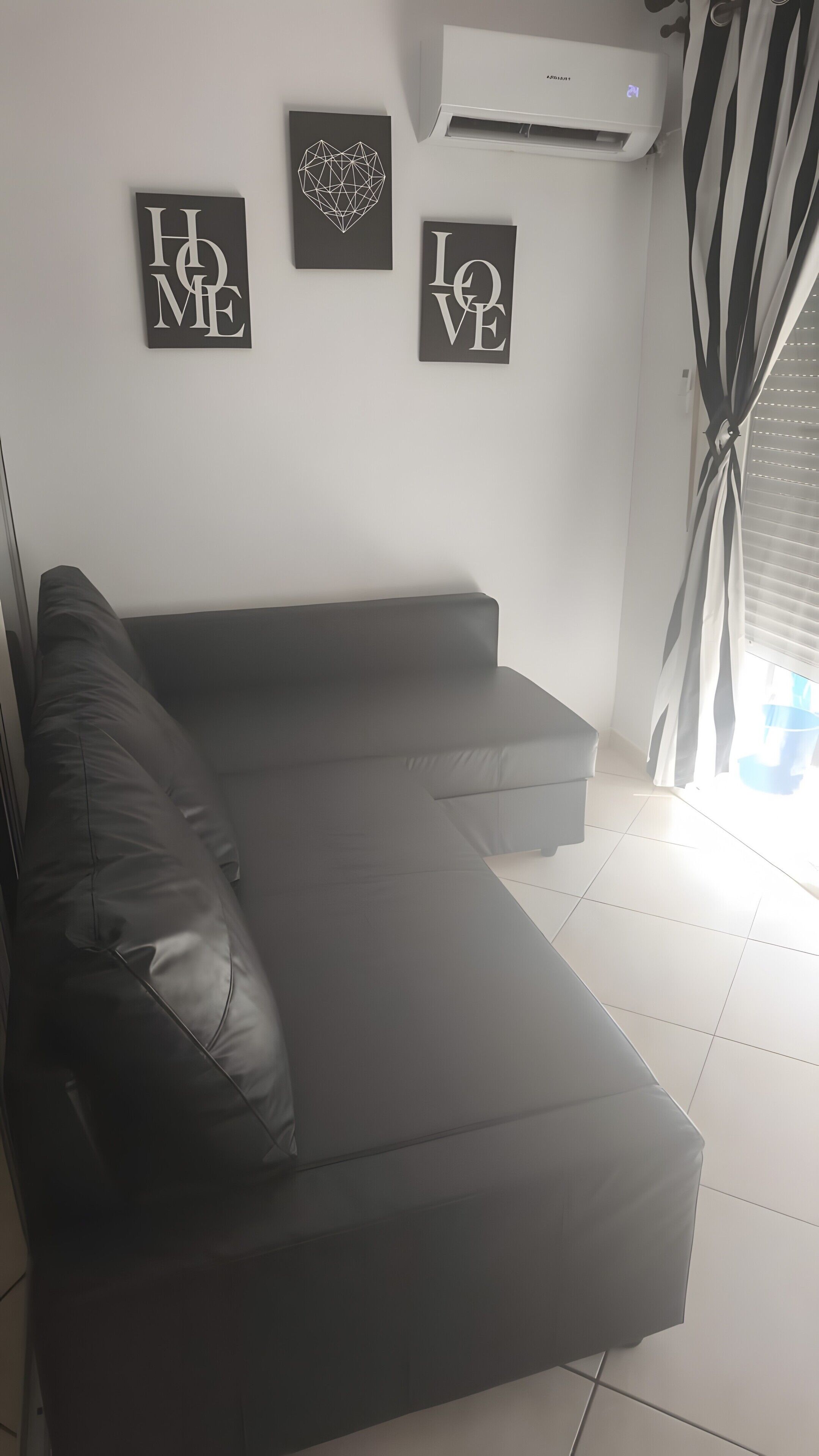 Un salón moderno con un sofá gris, un aire acondicionado de pared y tres obras de arte enmarcadas con frases motivacionales.