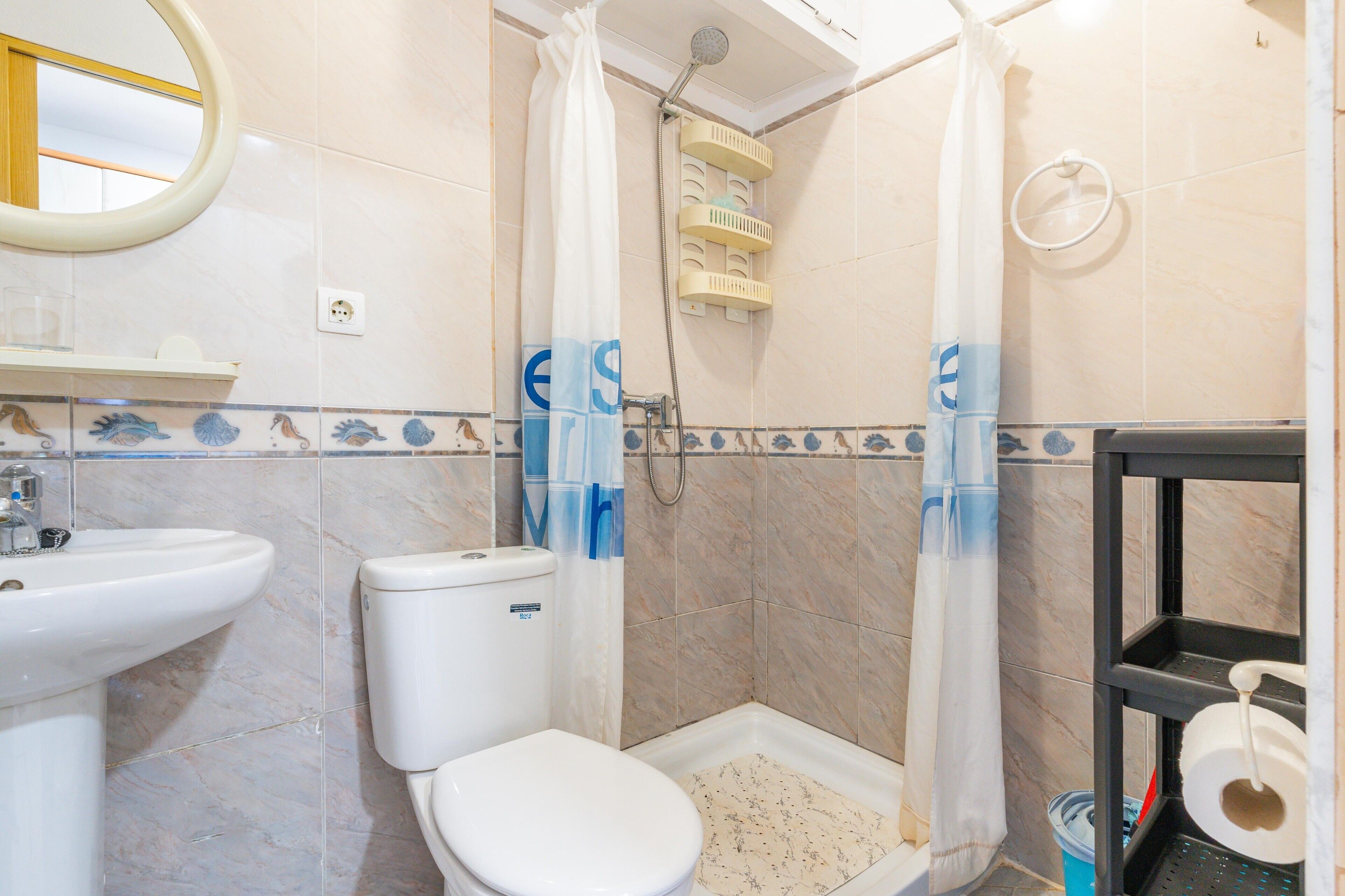 A bathroom with a toilet, sink, shower, and a shelf with toiletries.