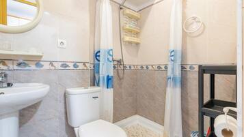 A bathroom with a toilet, sink, shower, and a shelf with toiletries.