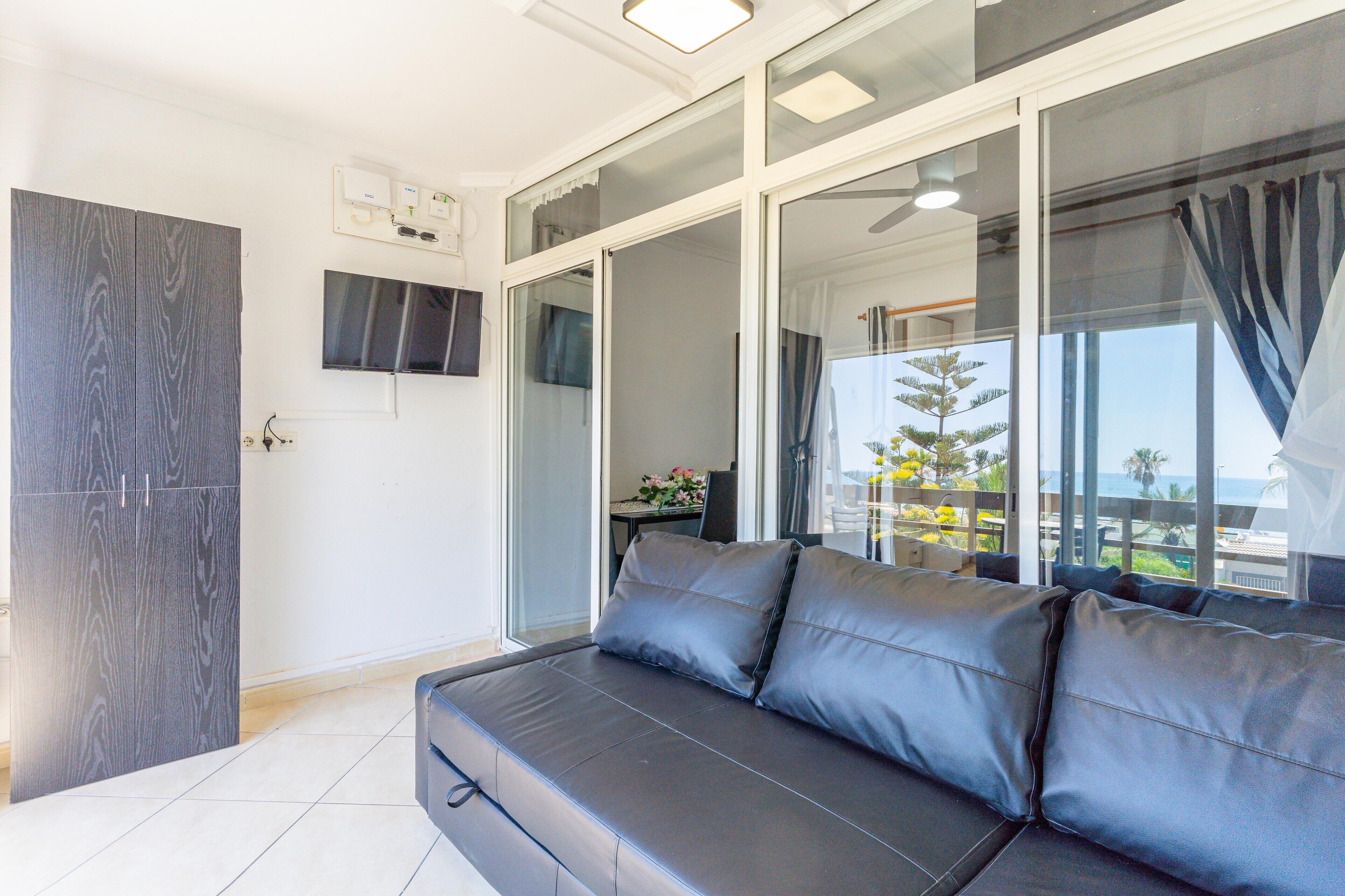 Una sala de estar moderna con un sofá, un televisor y un ventanal corredera que da a un balcón con vistas.